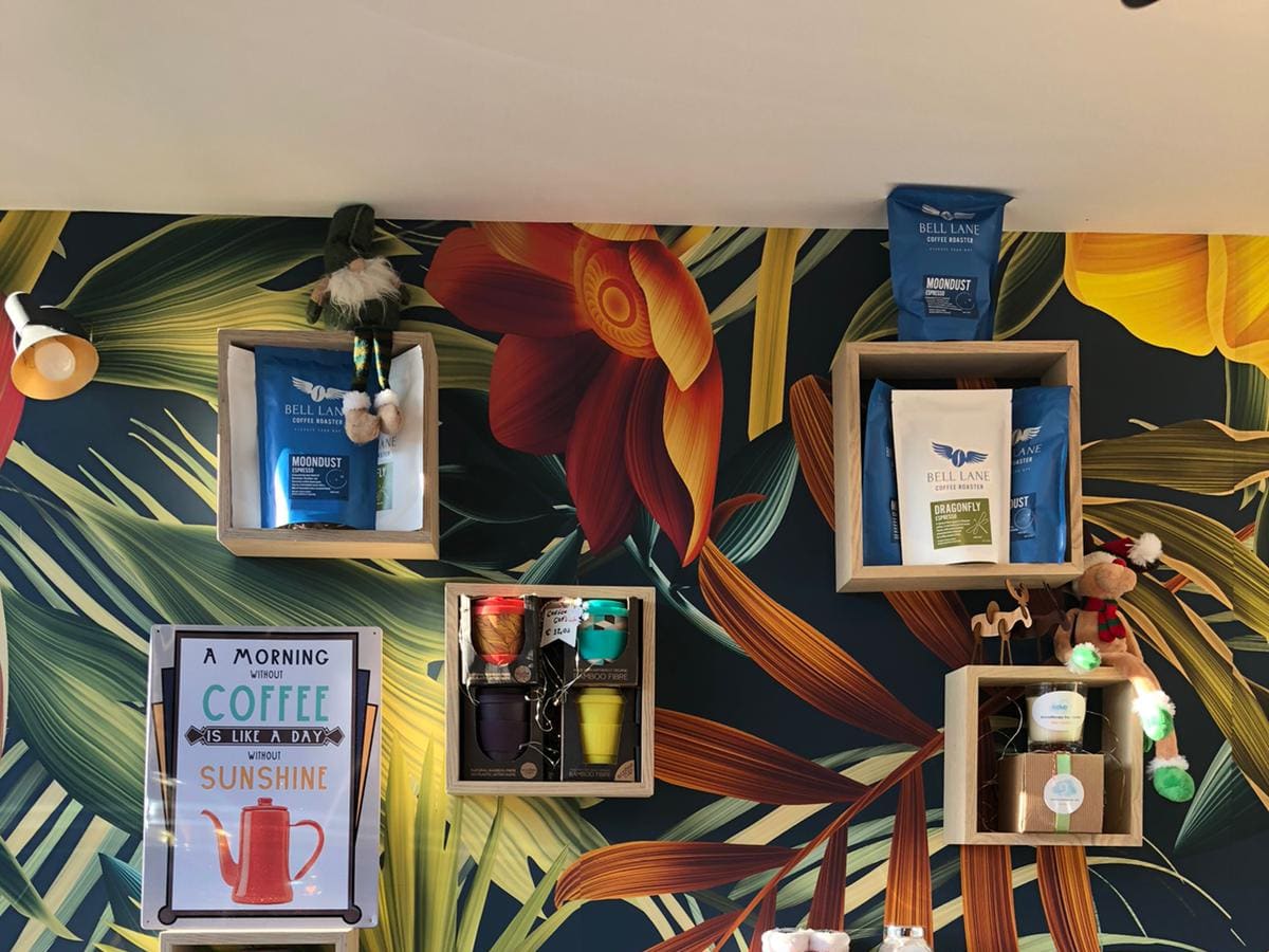 Bags of Bell Lane Coffee Roaster espresso on the retail wall, against the kiosk's tropical mural