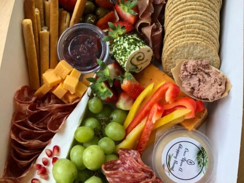 A charcuterie and grazing box with cheese, cured meats, crackers, grapes and dips